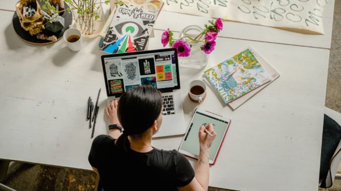 photo of woman writing on tablet computer while using laptop